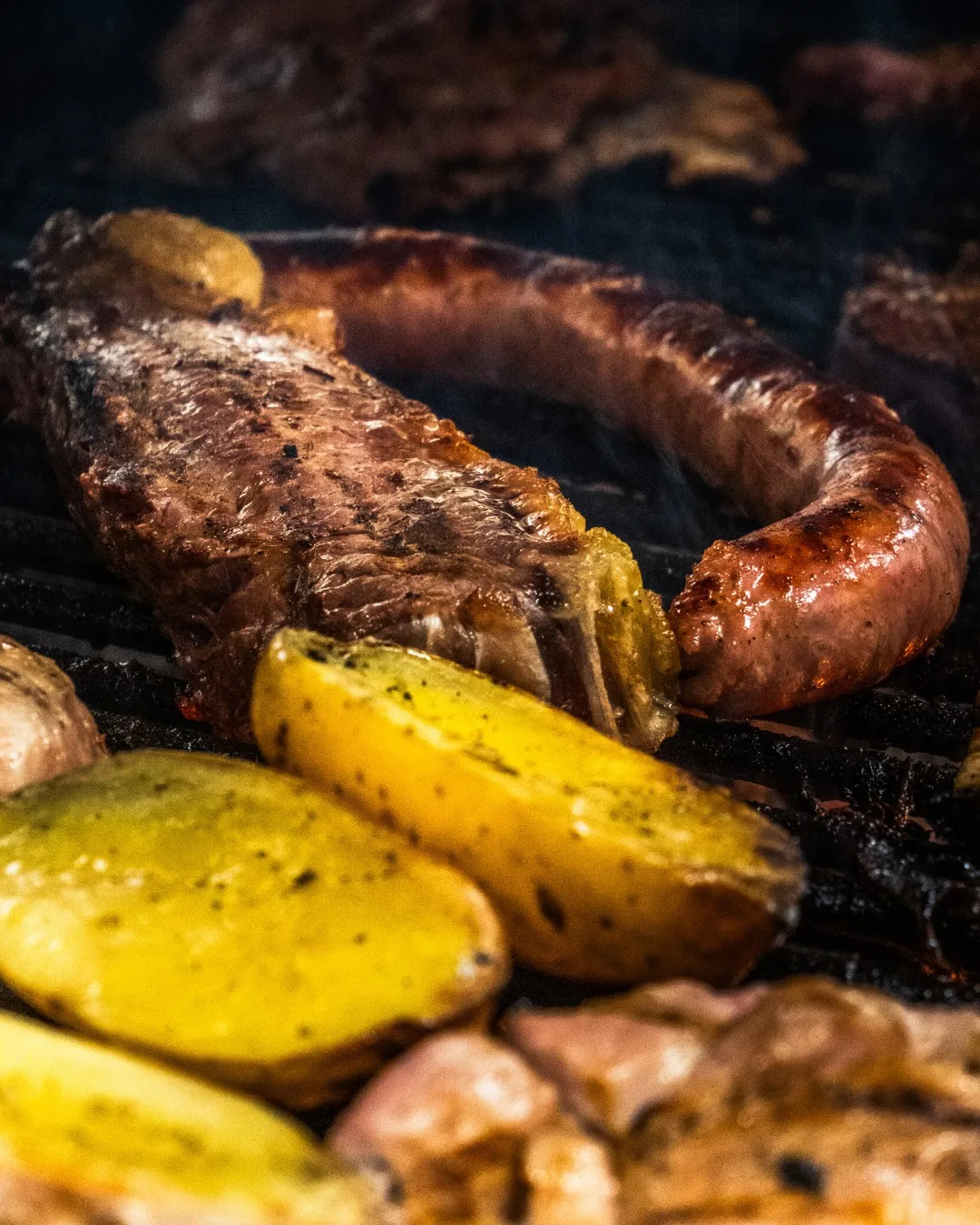 Carne y butifarra a la brasa con patatas asadas sobre la parrilla
