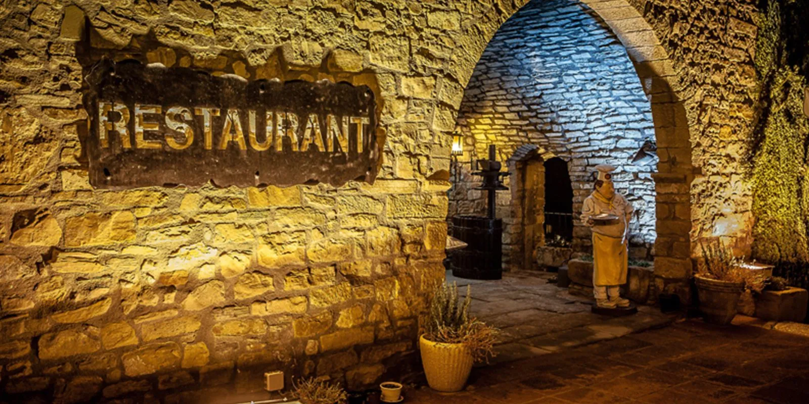 Entrada de piedra de Els Torrents iluminada de noche, con el rótulo Restaurant en el muro y un arco que da paso al patio